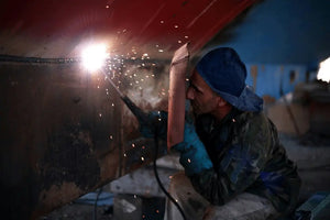 A welder is welding with a mask in one hand and a welding gun in the other